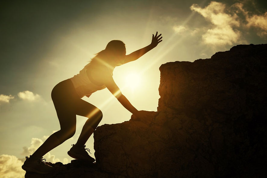 Uma mulher com traje esportivo escalando uma montanha com força e motivação em dia quente e ensolarado  